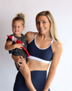happy mom holding her toddler while wearing the nursing sports bra in navy and white 